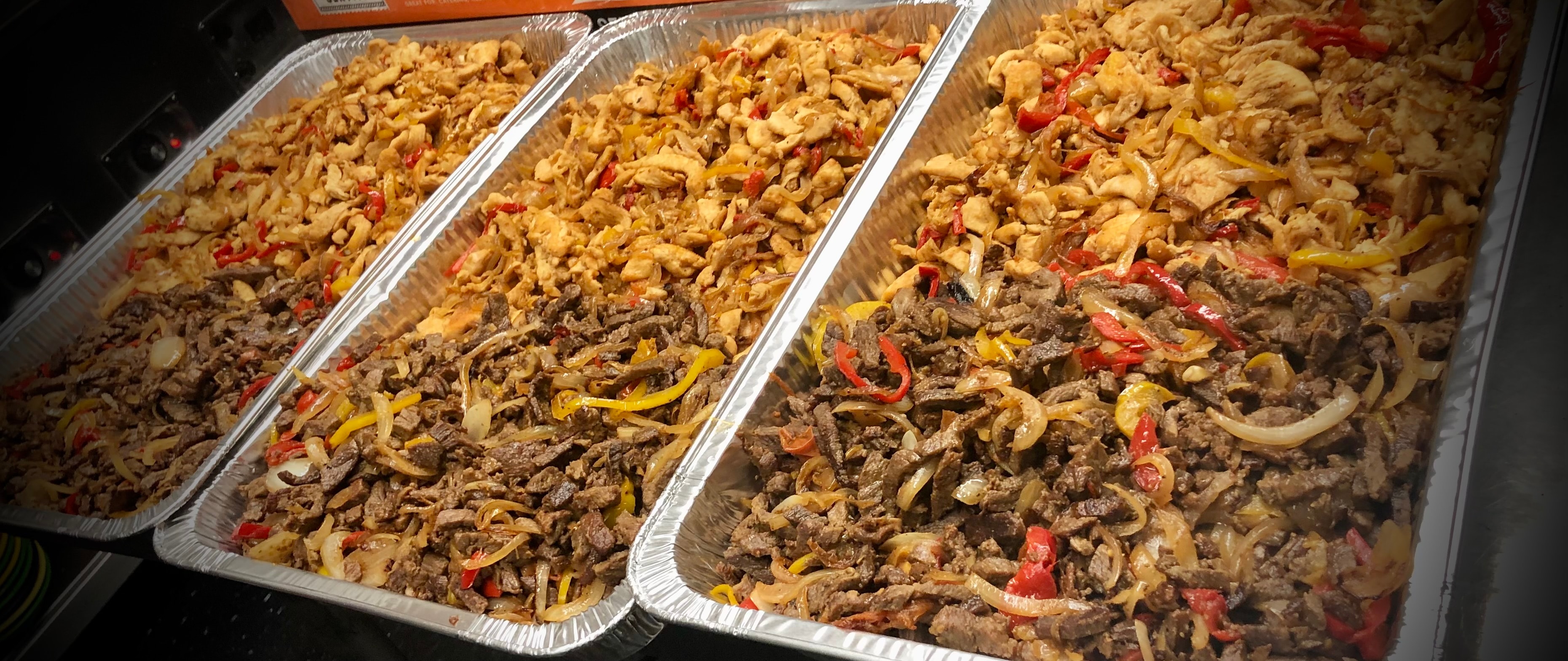 Large aluminum trays of grilled chicken and steak fajitas with peppers and onions — Salsas catering