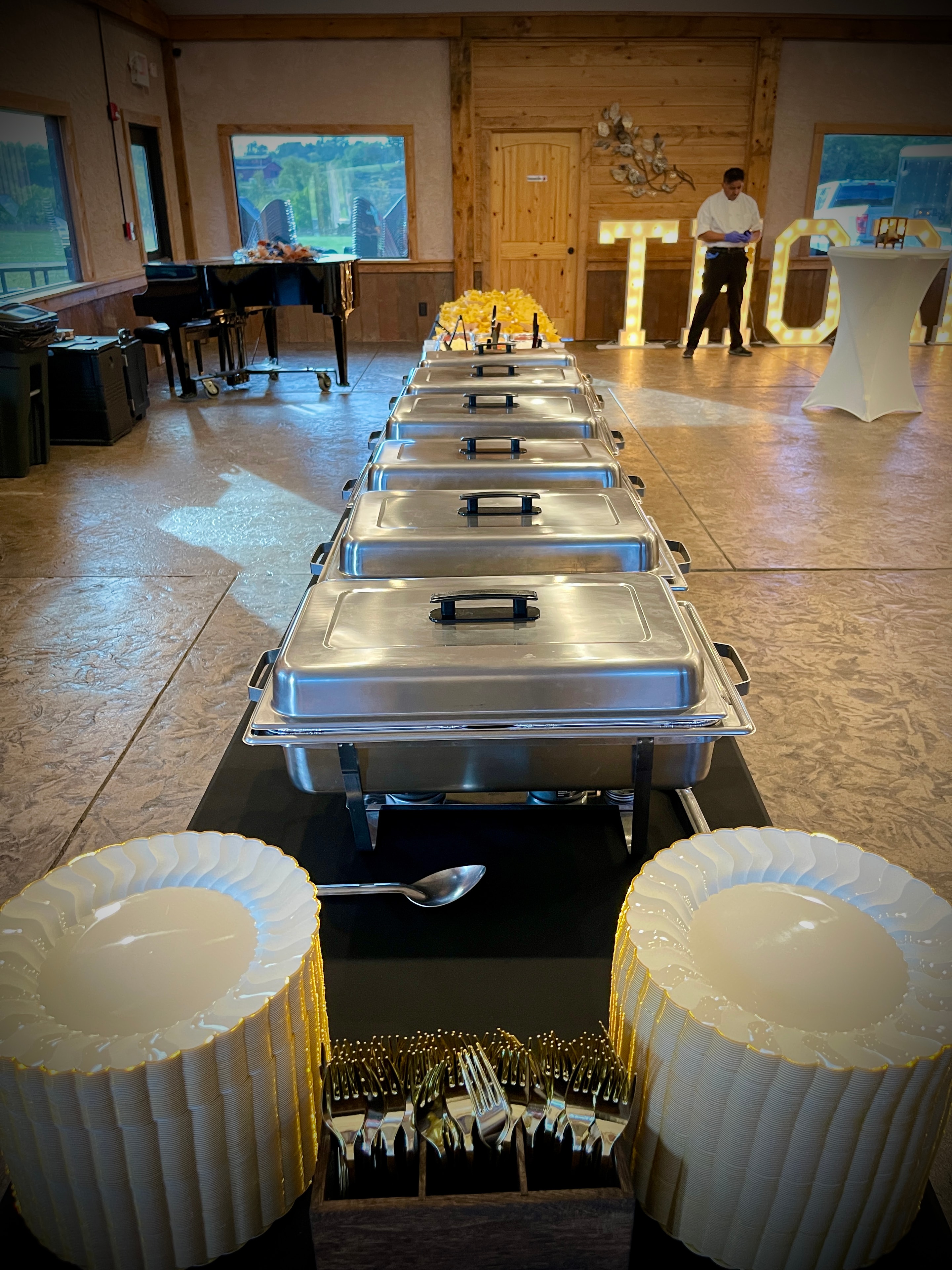 Row of polished chafing dishes lined up with stacked plates and gold flatware ready for service