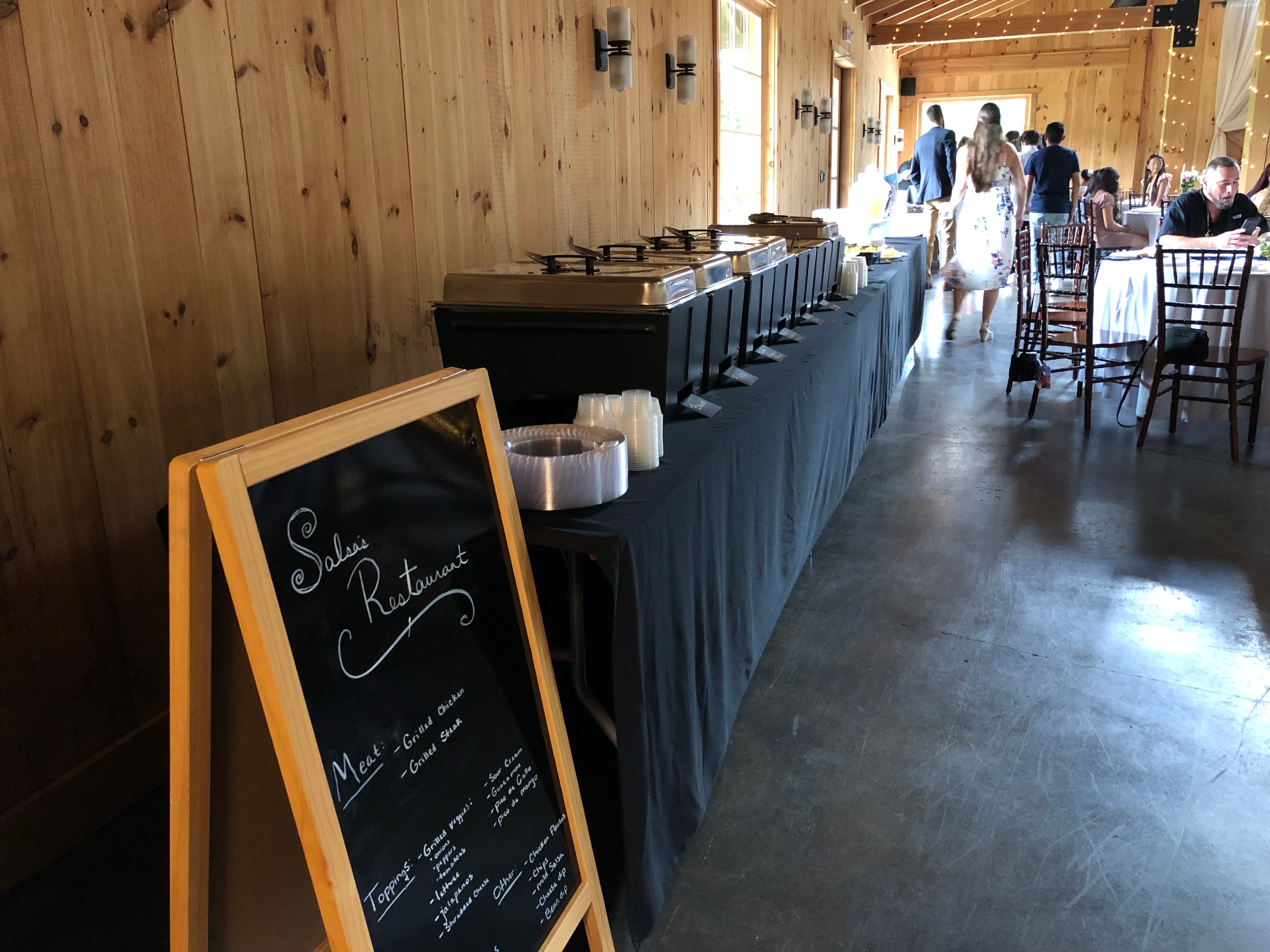 The Salsas Restaurant & Catering | Mexican catering setup at a barn wedding venue with chafing dishes and branded chalkboard sign
