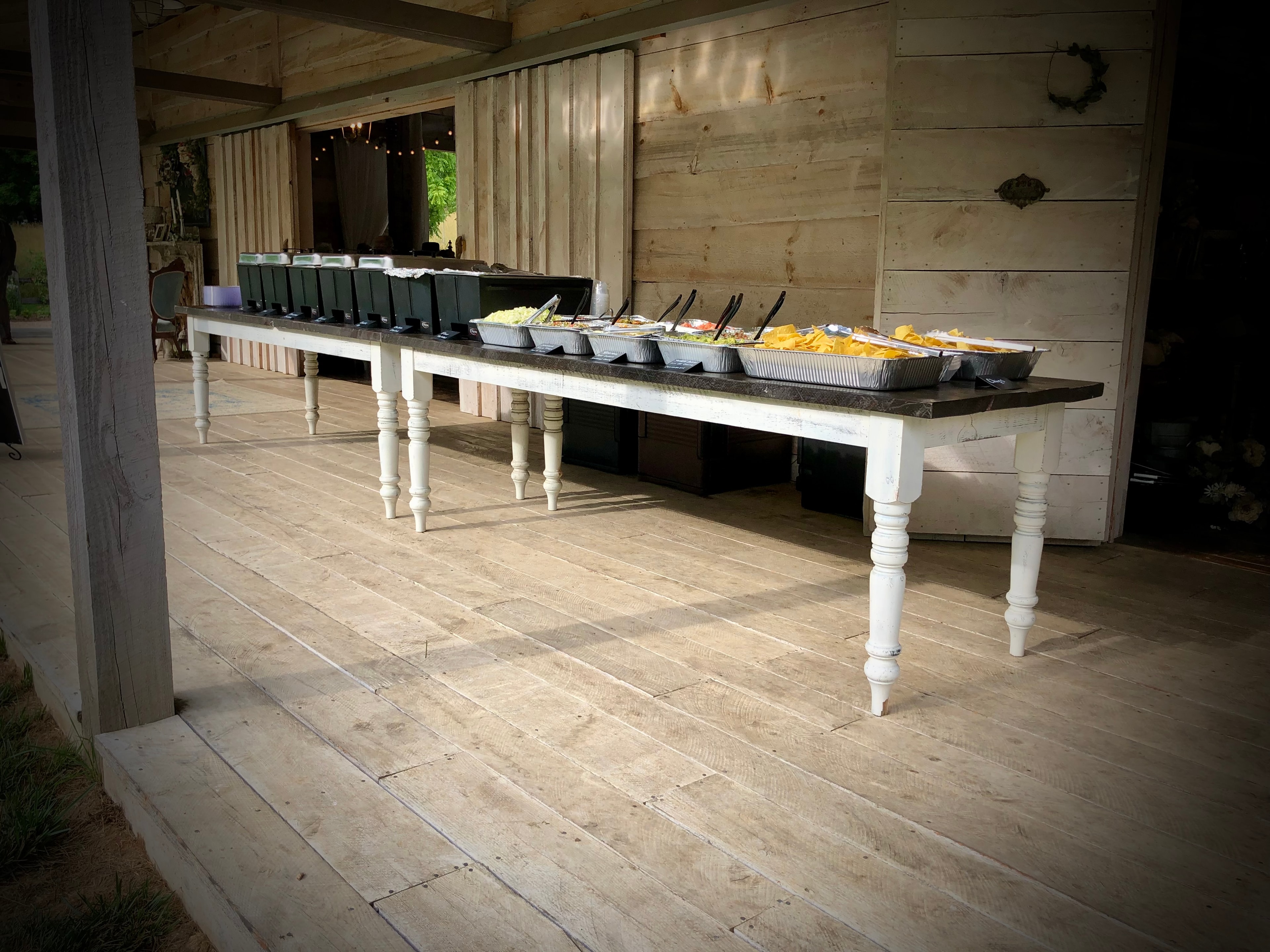 Outdoor catering buffet table on a rustic porch with food trays and chips ready for guests