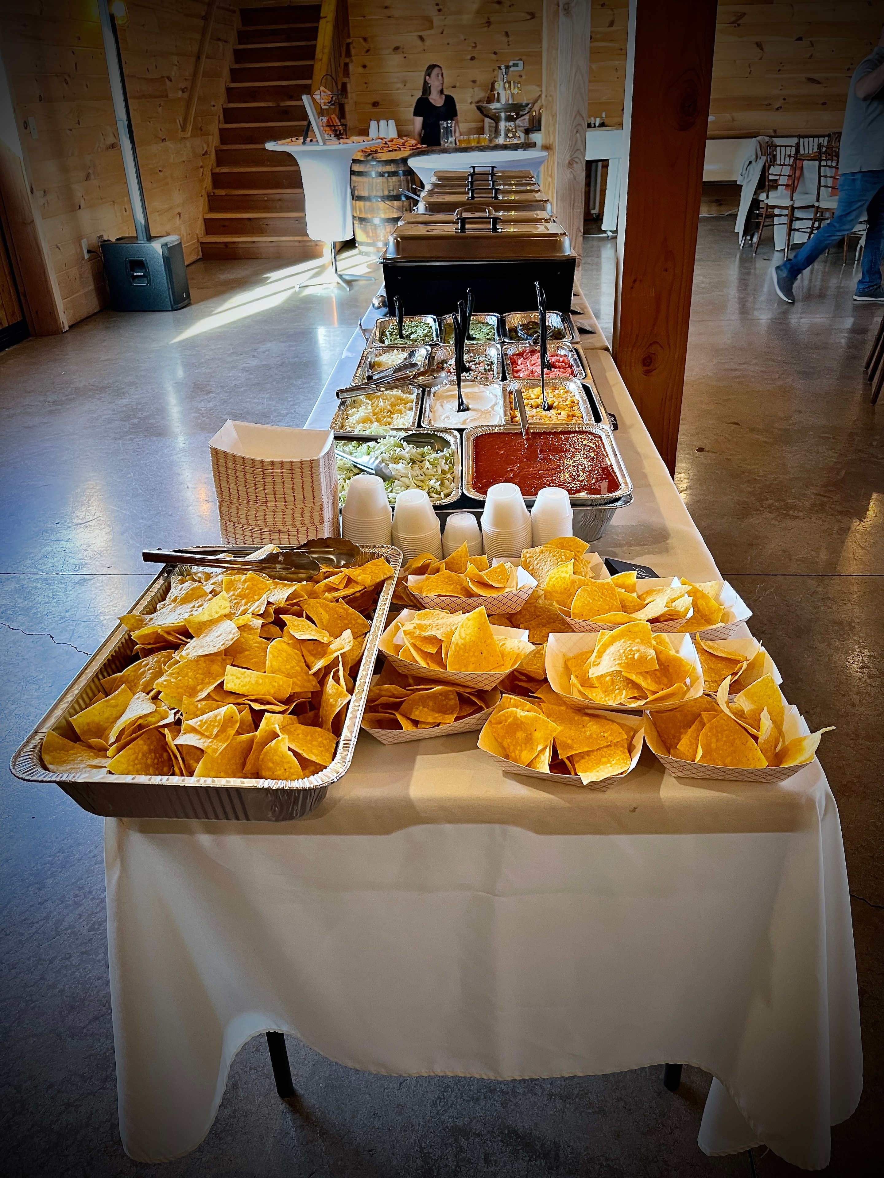 Full taco bar spread inside a barn venue with chips, salsa, guacamole and all the toppings