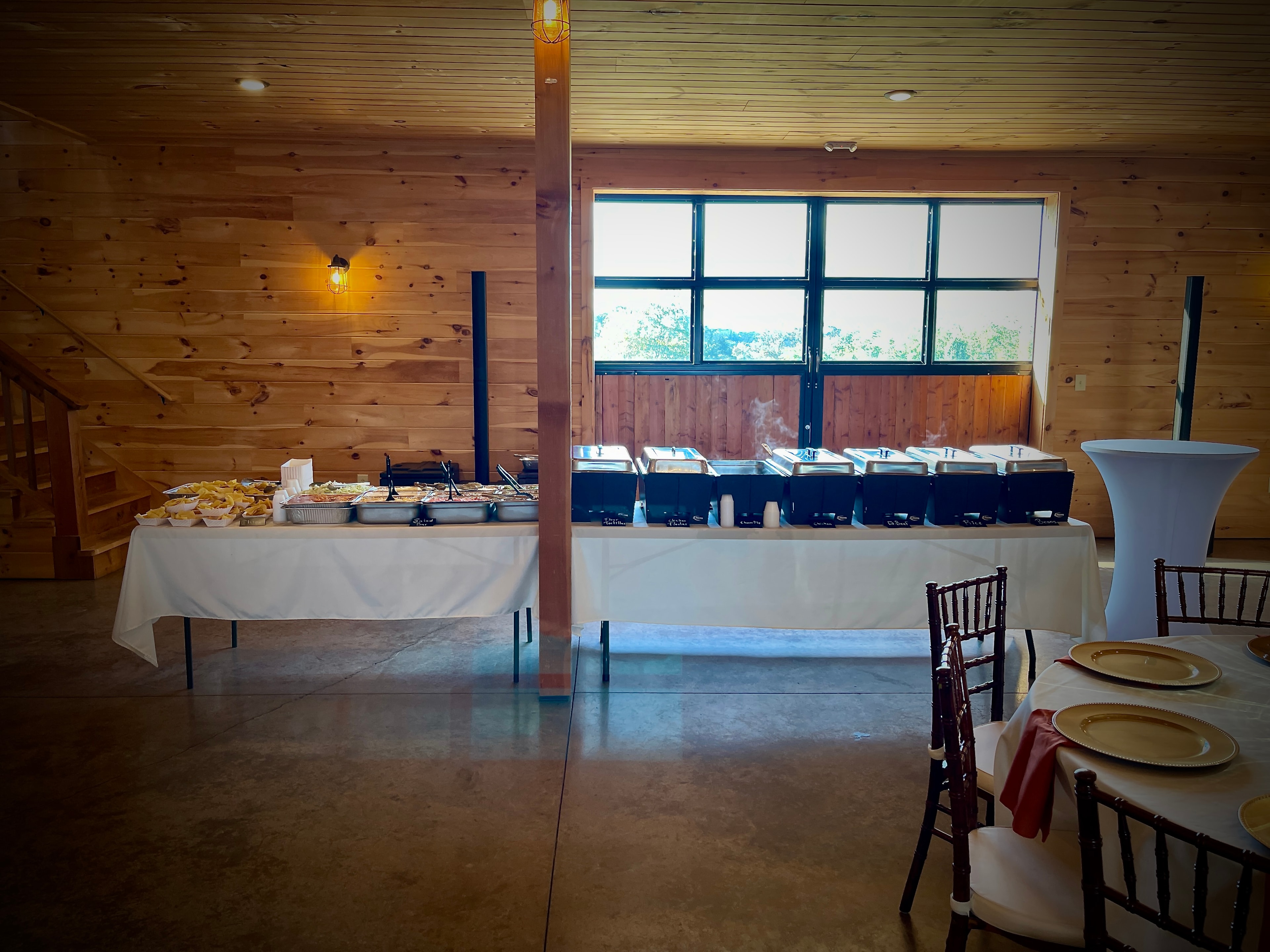 Wide view of Salsas catering buffet setup inside a bright barn with chafing dishes and place settings