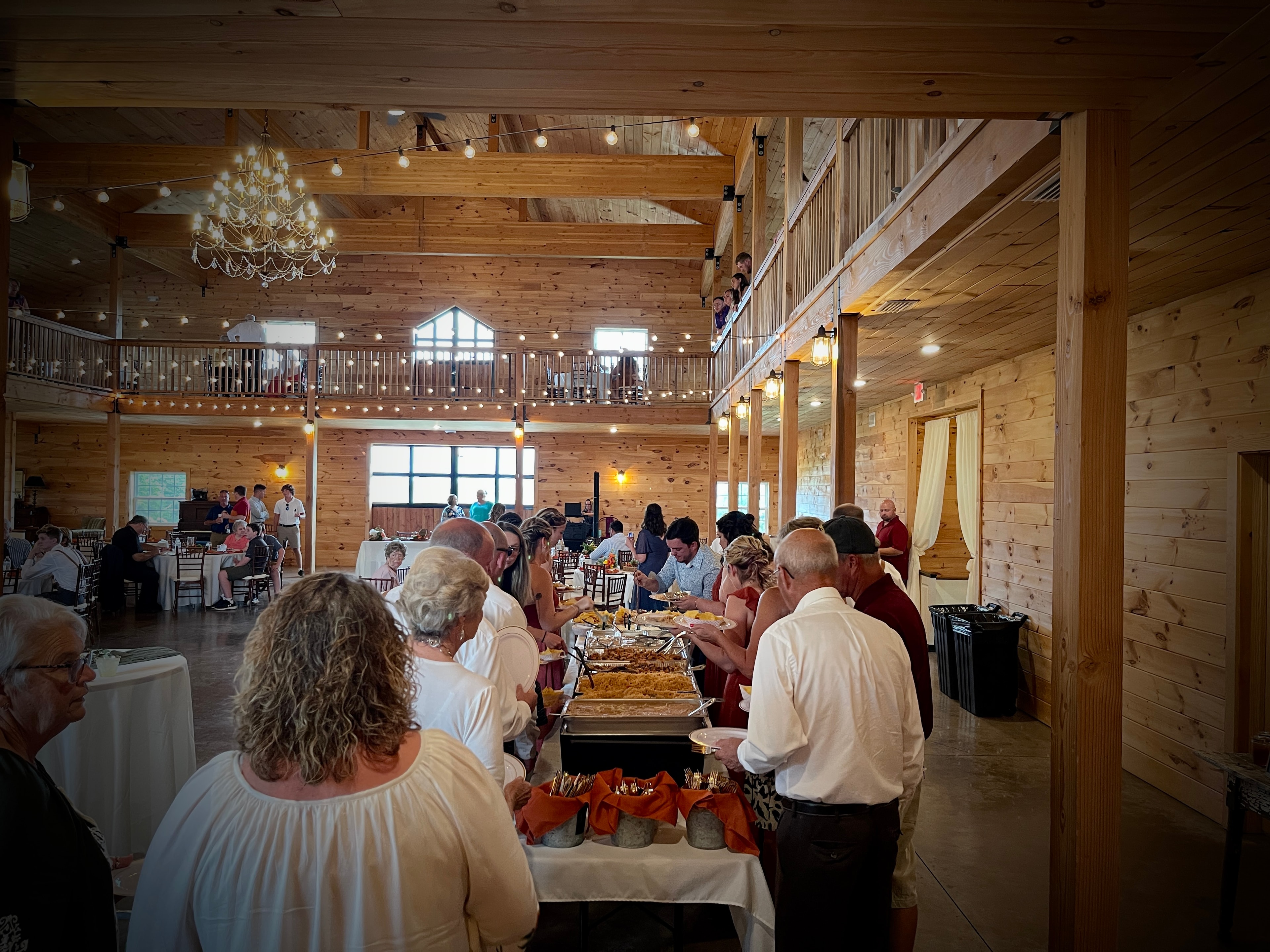 Wedding guests lining up at the Salsas catering buffet inside a beautiful barn venue with string lights