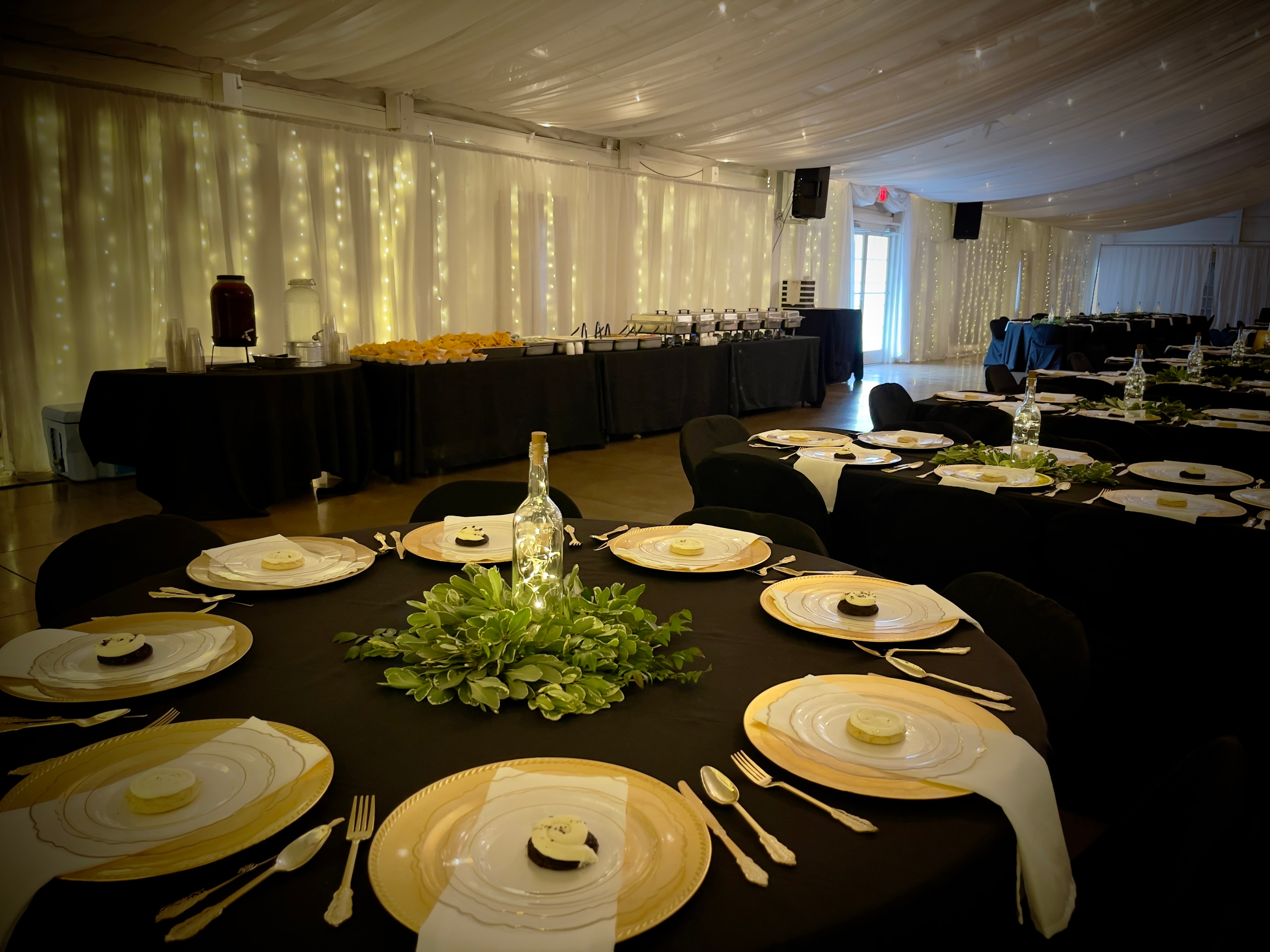 Elegant black-tablecloth event setup with gold charger plates and fairy light backdrop — Salsas catering